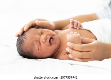 Newborn Baby Crying On White Bed While Mother’s Hands Takes Care Carefully. Family, Love And New Life Concept