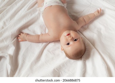 Newborn Baby In A Diaper Is Lying On His Back On A White Sheet. Products For Children, Toy. Concept Of A Happy Childhood And Motherhood. Child Care. Space For Text. High Quality Photo