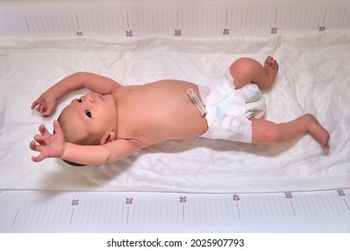 Ein Neugeborenes in Windeln auf einem weiß wechselnden Tisch mit einem Lineal mit Moro-Reflex