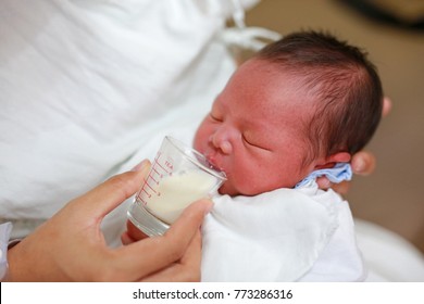 Newborn Baby Drinking Milk From Glass Cup.