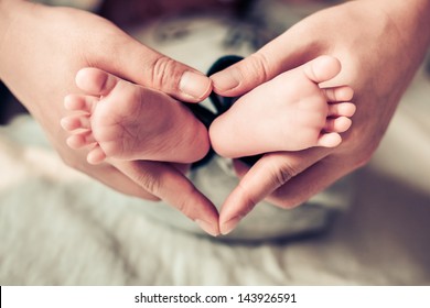 Newborn Baby Feet On Female Hands