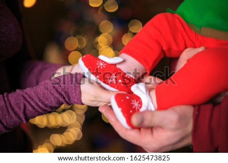 Newborn baby feet in parents hands on background of Christmas tree lights. Cute little infants in red shoes Close up. Feet of baby in mother's hands. little sweet newborn feets. parenthood concept.