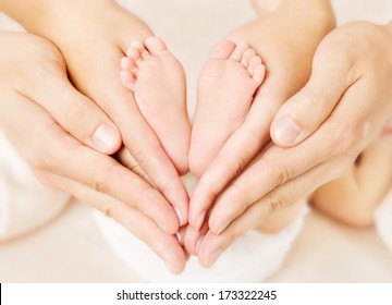 Newborn Baby Feet Parents Holding In Hands. New Born Kind And Love Symbol As Heart Sign.