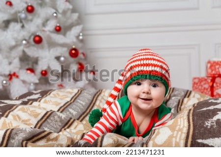Newborn baby girl dressed in gnome costume lying on white fur carpet among christmas decorations. Christmas photo of infant in ctriped cap. New Year concept.