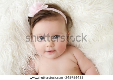 Newborn baby girl posed in a bowl on her back, on blanket of fur, smiling looking at camera