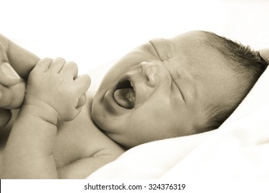 Newborn Baby Girl Wrapped In White Blanket Crying And Holding Her Mom's Hands