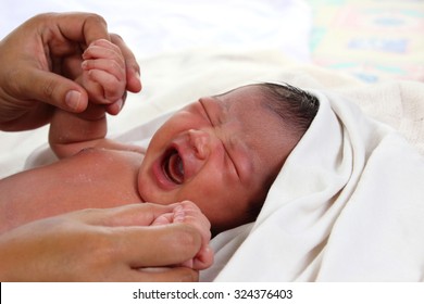 Newborn Baby Girl Wrapped In White Blanket Crying And Holding Her Mom's Hands