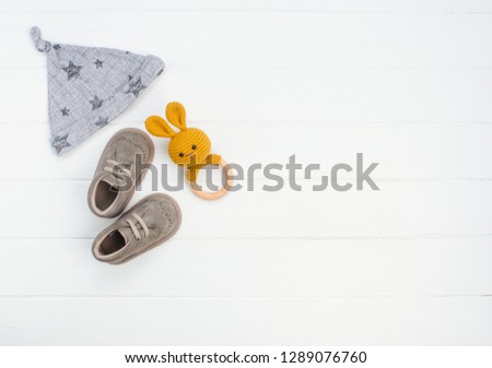 Newborn baby hat, shoes and rabbit beanbag on white wooden background with blank space for text. Top view, flat lay.