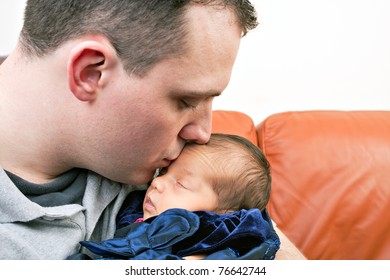 A Newborn Baby Is Held By Her Dad As He Kisses Her Cheek.