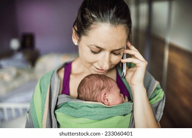 Newborn Baby Hold By Mother In The Baby Wrap Carrier. Mum Calling At The Phone.