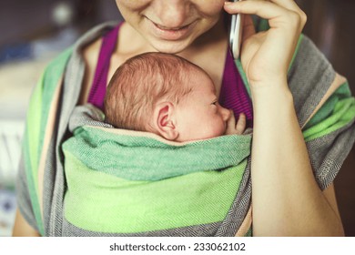 Newborn Baby Hold By Mother In The Baby Wrap Carrier. Mum Calling At The Phone.