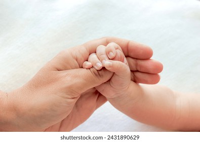 Newborn baby holds the thumb of his mother's hand on white background