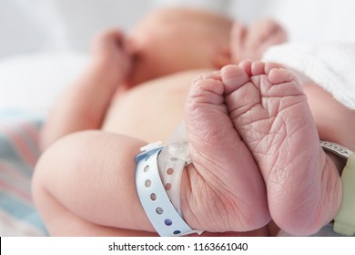 Newborn baby in hospital bed lying on their back with hospital bracelets on his feet.