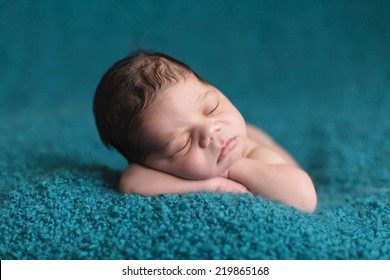 Newborn baby with lots of hair sleeping on a teal blanket