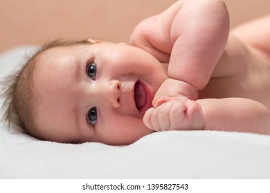 Newborn Baby Lying On Its Side And Smiling On A White Sheet And Looking Up