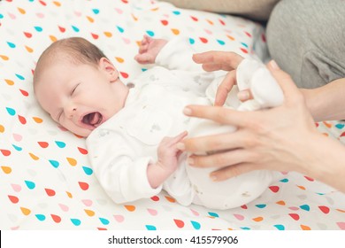 Newborn Baby Screaming In Pain With Colic; Mother Helping Her To Bend Her Knees To Ease Pain In Stomach