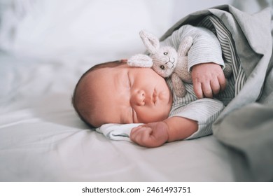 Newborn baby sleep at first days of life. Portrait of new born child boy one week old sleeping peacefully with a cute soft toy in crib in cloth background. - Powered by Shutterstock