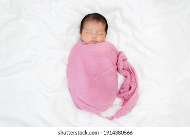 Newborn Baby Sleep In Pink Cloth Wrap Blanket On A Bed