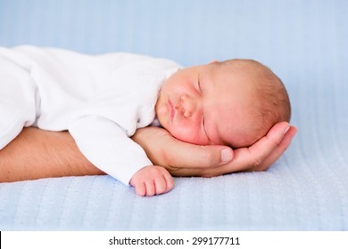 Newborn Baby Sleeping In Arms Of His Father. Dad Holding New Born Son. Child Taking A Nap On Parent Hand. Infant Kid Sleeping On A Blue Blanket. Textile Bedding For Kids. Parents And Children Bonding.