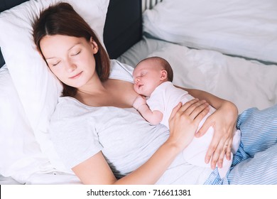 Newborn Baby Sleeping In The Hands Of His Mother. Image Of Happy Maternity And Co-sleeping. Mom And Child's First Month Of Life At Home.