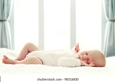 Newborn baby sleeping on white blanket in front of a window. Soft focus, very shallow DOF.
