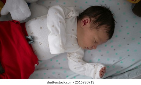 Newborn baby sleeping peacefully on a soft, star-patterned blanket, dressed in a white onesie with tiny triangle prints and red pants, conveying innocence and tranquility - Powered by Shutterstock