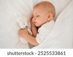 a newborn baby sleeps sweetly holding a toy in his hands, a place for text, a baby sleeps on a white bed under a blanket with a pen under his cheek, a healthy baby