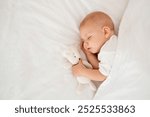 a newborn baby sleeps sweetly holding a toy in his hands, a place for text, a baby sleeps on a white bed under a blanket with a pen under his cheek, a healthy baby