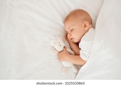 a newborn baby sleeps sweetly holding a toy in his hands, a place for text, a baby sleeps on a white bed under a blanket with a pen under his cheek, a healthy baby's sleep.