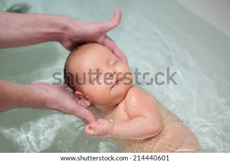 Newborn  baby swimming with help of parents hands for the first time. Baby has neonatal jaundice. Focus on baby head