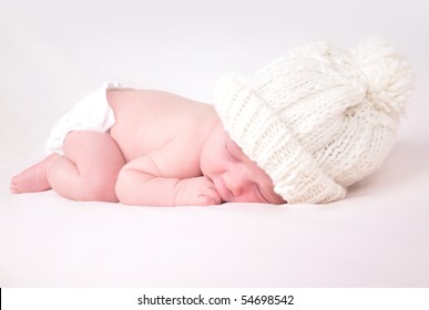 A Newborn Baby Is Wearing A White Hat And Laying Down Sleeping On A Soft White Background. Use The Photo To Represent Life, Parenting Or Childhood.