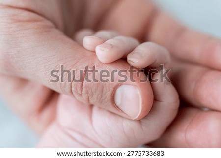 Newborn baby's tiny hand protectively grasping an adult's finger symbolizing love and family bond