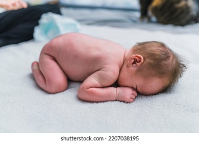 Newborn Boy With Brown Hair Laying On His Tummy In A Fetal Position And Hiding His Face During Changing A Diaper. High Quality Photo