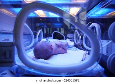 Newborn child baby having a treatment for jaundice under ultraviolet light in incubator. A neonatal intensive care unit (NICU), intensive care nursery (ICN) for premature newborn infants