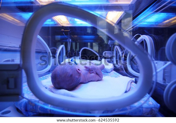 Newborn child\
baby having a treatment for jaundice under ultraviolet light in\
incubator. A neonatal intensive care unit (NICU), intensive care\
nursery (ICN) for premature newborn\
infants