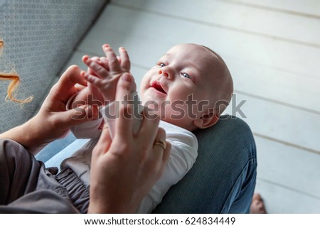 Newborn child lies on his mother's lap. Mother holding her newborn child. Woman and new born boy relax in a white bedroom. Mother breast feeding baby. Family at home