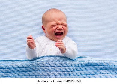 Newborn crying baby boy. New born child tired and hungry in bed under blue knitted blanket. Children cry. Bedding for kids. Infant screaming. Healthy little kid shortly after birth. Cable knit textile - Shutterstock ID 340818158