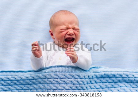 Newborn crying baby boy. New born child tired and hungry in bed under blue knitted blanket. Children cry. Bedding for kids. Infant screaming. Healthy little kid shortly after birth. Cable knit textile