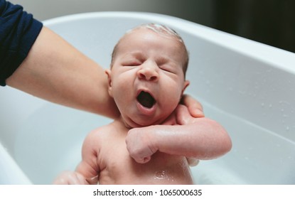Newborn girl yawning in the bathtub held by her mother