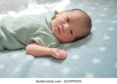 Newborn Male Baby Looking Up At The Camera While Lying On A Blanket Of Stars