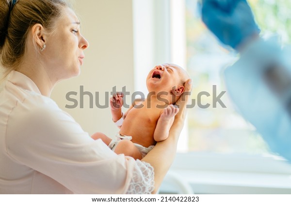 Newborn physical exam. First moments of\
bonding. Mother caressing and calming down her crying newborn baby\
daughter in hospital.