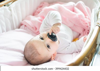 newborn pink cradle hold black pacifier hand looking camera portrait background candid