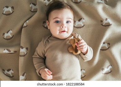 Newborn Toddler Boy In Beige Bodysuit Plays With Wooden Toy Top View