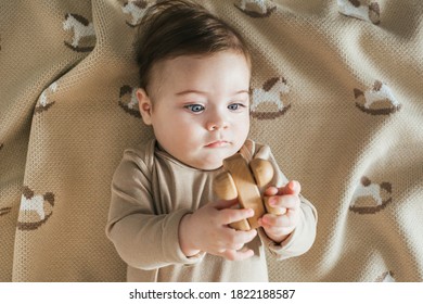 Newborn Toddler Boy In Beige Bodysuit Plays With Wooden Toy Top View