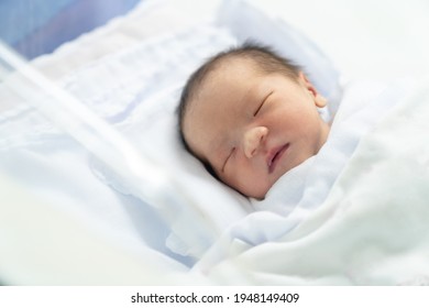 The Newborn Is Wrapped In A White Diaper In A Baby Crib In A Hospital Nursery Room.