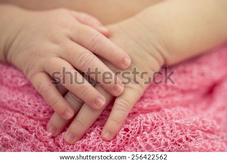 A newborn's hand against a pink blanket.