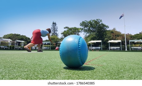 Newcastle, Australia - Feb 2020: View Of The Blue Lawn Bowls Balls On Green Synthetic Lawn With Female Bowler In Action From Behind. Lawn Bowling Is A Outdoor Sport At Australia