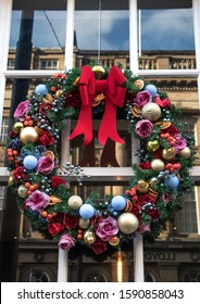 Newcastle / Great Britain - December 14, 2019 : Winter Christmas Yule Wreath On A Window With Big Red Bow, Flowers And Baubles