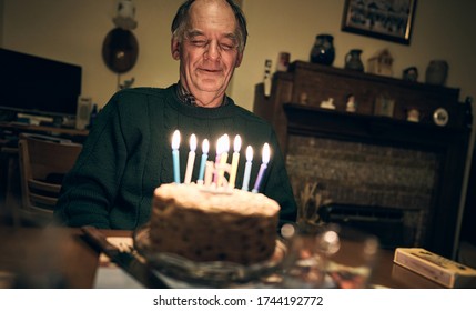 NEWCASTLE UPON TYNE, ENGLAND, UK - NOVEMBER 24, 2018: A Senior Adult Male Siting Back Making A Wish Before Blowing Out The Lit Candles On His Fruit Birthday Cake.