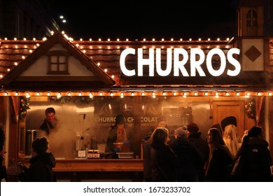 Newcastle Upon Tyne, UK - December 2019: Customers Lining Up In Front Of A Churros Shop Which Has A Festive Design And Its Shop Keeper Is Smiling While Preparing The Churros For Customers